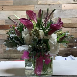 Pink calla lilies and white hydrangeas in a glass vase with a pink ribbon