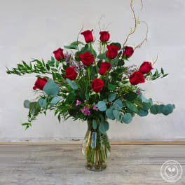 Red roses arranged in a clear glass vase with eucalyptus and filler flowers