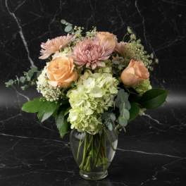 Peach roses and pink blooms in a clear glass vase