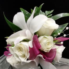 White roses and calla lilies arranged in a glass vase with magenta ribbon accents.