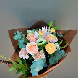 Bouquet of peach and yellow roses with eucalyptus in brown paper