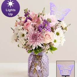 Pink and white mixed bouquet in a purple glass vase with a butterfly light