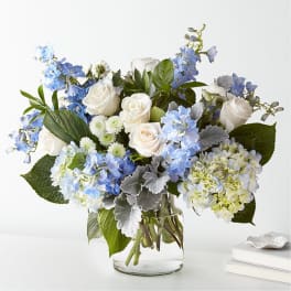 White roses and blue flowers arranged in a clear glass vase