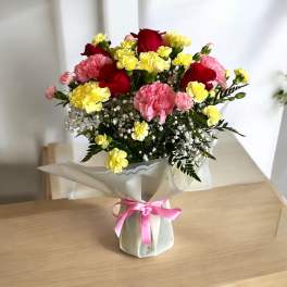 Bouquet of red roses, pink carnations, and yellow spray flowers wrapped in white paper