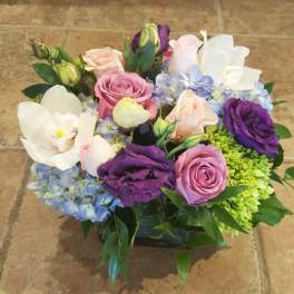 Mixed bouquet of roses, orchids, and hydrangeas in a low container