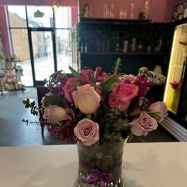 Pink and lavender roses arranged in a glass vase with a purple ribbon