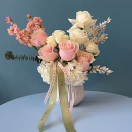 Pink and white roses arranged in a ribbed vase with ribbon tails