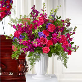 Bright pink and purple floral arrangement in a white vase beside a casket