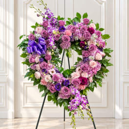 Heart-shaped floral wreath with purple and pink roses on a stand