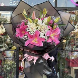 Large bouquet of pink and white lilies with baby's breath wrapped in black paper with pink ribbons