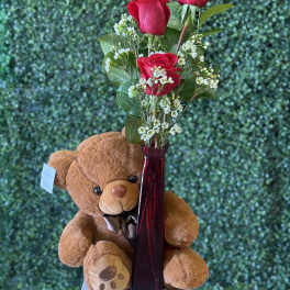Red roses in a tall vase with a teddy bear