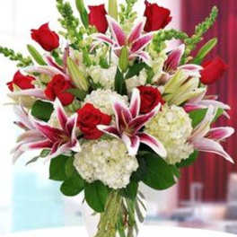 Bouquet of red roses, pink lilies, and white hydrangeas in a glass vase