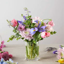 Mixed bouquet of pink, purple, and white flowers in a clear glass vase