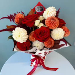 Bouquet of red roses, white dahlias, and peach blooms wrapped in patterned paper