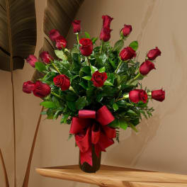 Red roses arranged in a black vase with a large red ribbon