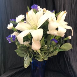 White lilies and purple filler flowers in a blue glass vase