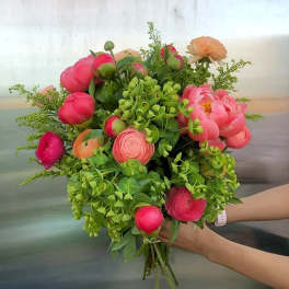 Handheld bouquet of pink and peach flowers with lush greenery