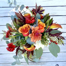 Mixed bouquet of orange roses, red blooms, and eucalyptus in a glass vase