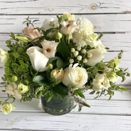 Round arrangement of white and cream flowers with soft green accents in a clear glass vase.