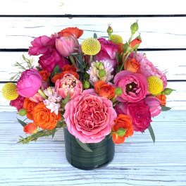 Bright arrangement of pink and orange roses, ranunculus, and tulips in a green glass vase