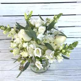 White flower arrangement with roses, hydrangea, and snapdragons in a clear glass vase