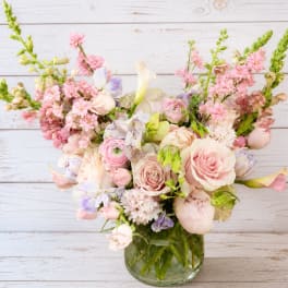 Pastel bouquet of roses, calla lilies, and mixed blooms in a glass vase