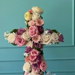 Cross-shaped floral arrangement of roses and pink blooms on a stand