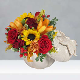 Bouquet of red roses, sunflowers, and orange lilies in a white pumpkin vase