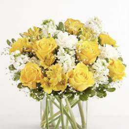 Yellow roses and white flowers arranged in a clear glass vase
