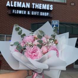 Hand-tied bouquet of pink peonies with white filler flowers wrapped in white paper with a pink ribbon.
