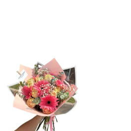 Handheld bouquet of pink gerbera daisies and peach roses wrapped in pink paper