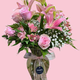 Pink roses and lilies arranged in a glass vase with a ribbon