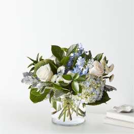 White roses and blue flowers in a clear glass vase