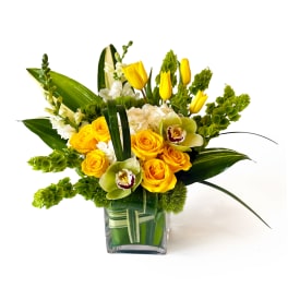 Yellow roses and tulips in a glass vase with white orchids