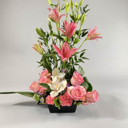 Tall floral arrangement with pink lilies, roses, and white orchids in a black vase