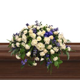 Large white and purple floral spray on a wooden casket