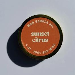 Round candle tin labeled "sunset citrus" on a plain surface