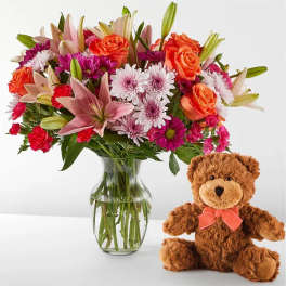 Mixed bouquet in a glass vase beside a teddy bear