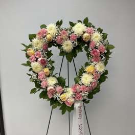 Heart-shaped floral wreath with pink and white flowers on a stand