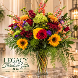 Mixed bouquet of roses, sunflowers, and mums in a clear glass vase
