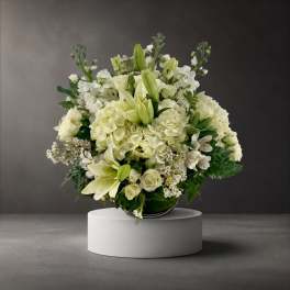 White floral arrangement with lilies, roses, and hydrangeas in a low vase