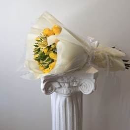 Bouquet of yellow roses and pale flowers wrapped in cream paper
