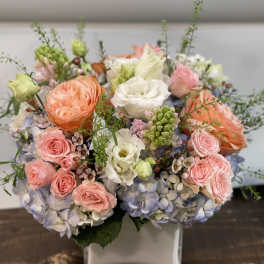 Pastel bouquet of roses, hydrangeas, and white blooms in a square vase