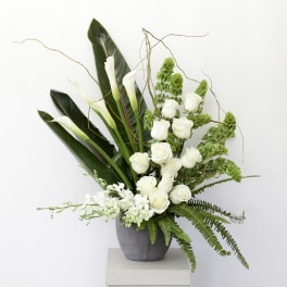 White roses and calla lilies in a gray vase with green foliage