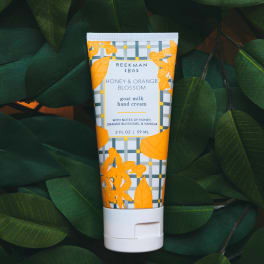 Tube of honey and orange blossom hand cream on dark green leaves
