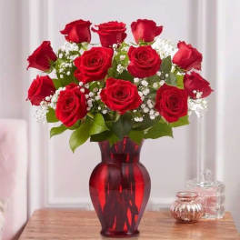 Red roses arranged in a red glass vase with white filler flowers