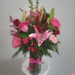 Pink and red floral arrangement in a glass vase with a pink ribbon