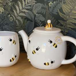 Bee-patterned ceramic mug and teapot on a wooden surface