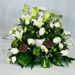 White lilies and roses arranged with green accents in a low centerpiece