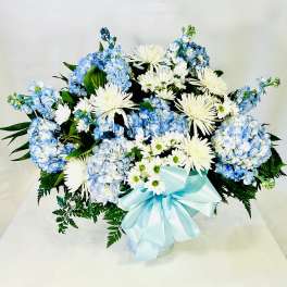 Blue hydrangeas and white chrysanthemums in a vase with a pale blue ribbon
